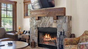 A stone fireplace with a TV above it, a comfortable seating area with a couch and a coffee table, and a window with blinds.