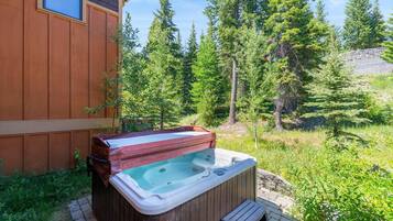 A wooden cabin with a hot tub in a forested area.