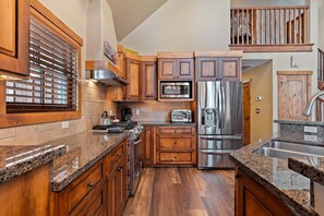 Cocina con armarios de madera, encimeras de granito y electrodomésticos de acero inoxidable, con una escalera a la vista.