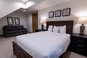 Une chambre à coucher avec un grand lit, un canapé de couleur sombre, deux tables de chevet avec des lampes et trois tableaux encadrés accrochés au mur.