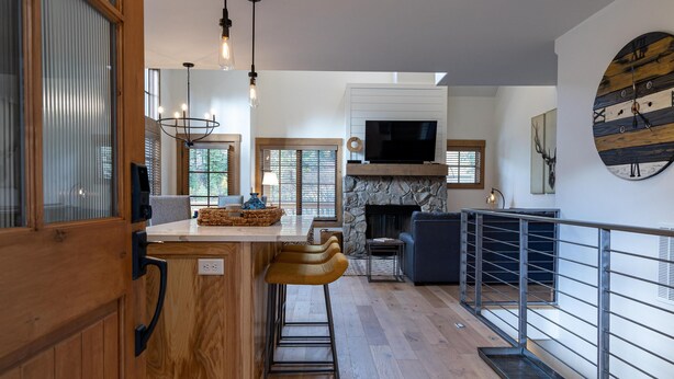 A modern kitchen with a stone fireplace, wooden bar stools, and a large TV. - Ideal 2 Bedroom Townhome  | Ski in/Ski Out (Tamarack)