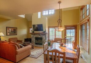 A living room with a fireplace, a dining table, and a television. - Mountainside Townhome, private Hot Tub, Pet Friendly (Tamarack)