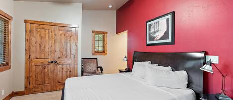 A bedroom with a bed, wooden wardrobe, a ceiling fan, a framed picture on the wall, and a nightstand with a lamp.
