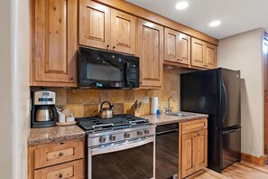 A kitchen with wooden cabinets, a stainless steel stove, a black refrigerator, and a microwave.