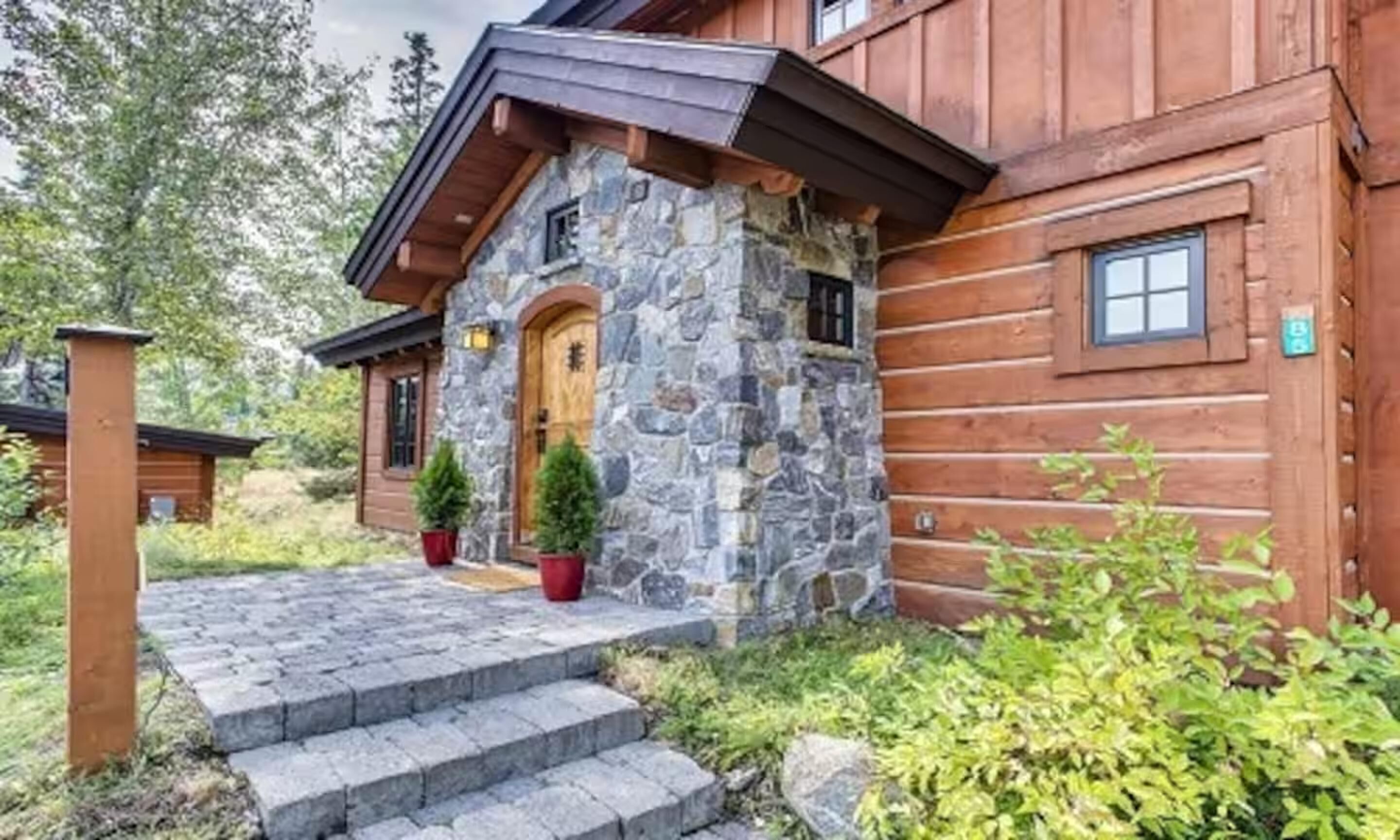 A log cabin with a stone entrance, wooden steps, and a small porch area.