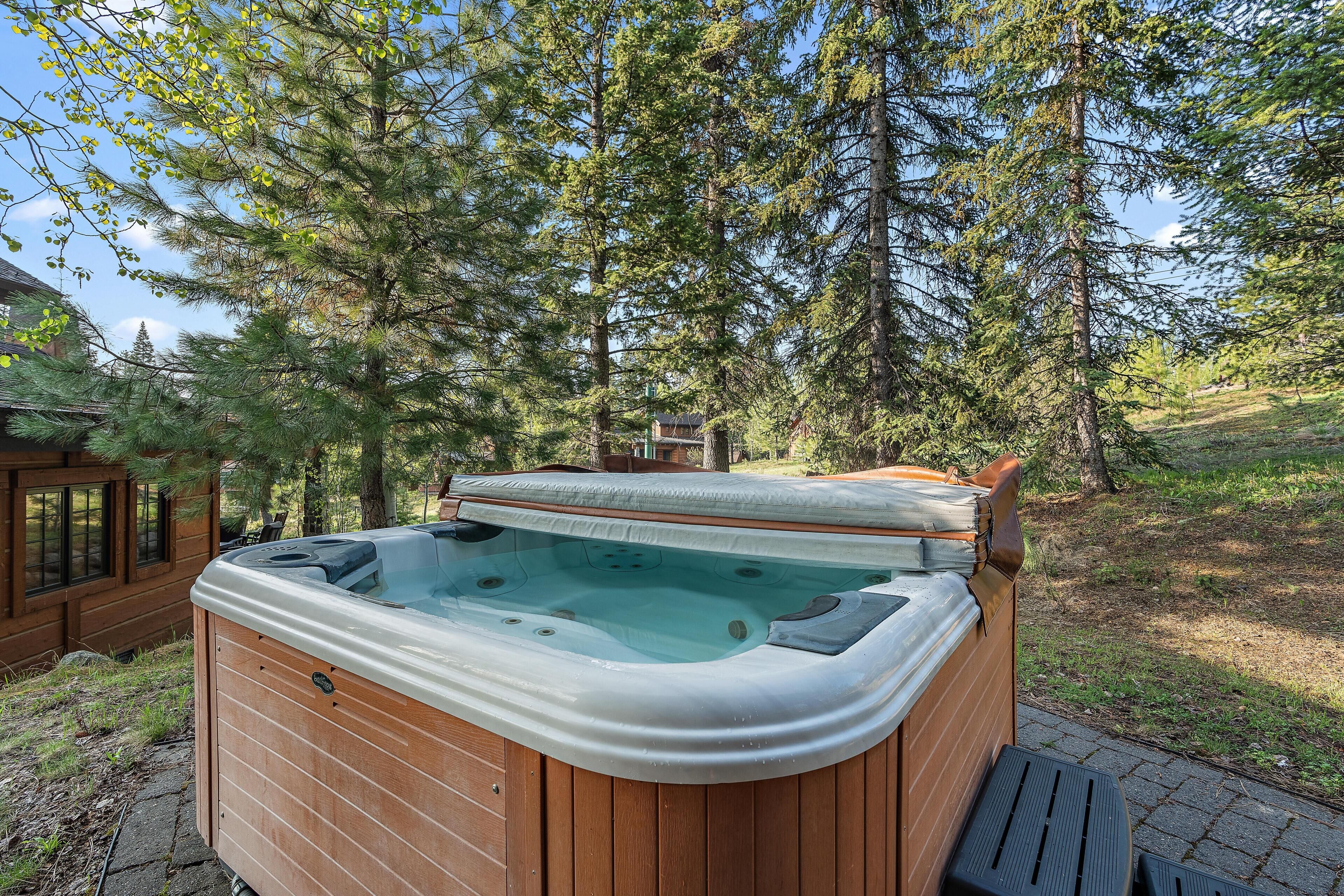 Een hottub in een bebost gebied, met een houten terras en een huis op de achtergrond.