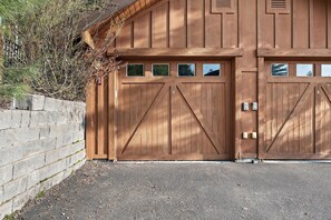 En trægarage med to store porte, en betonmur og en grusbelagt indkørsel.