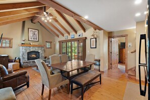 A spacious living room with a stone fireplace, wooden beams, and a large dining table. - Wonderful Cottage |Ski In/Out | Private Hot Tub (Tamarack)