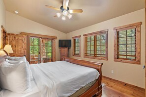 Une chambre à coucher avec un lit, une tête de lit en bois, un ventilateur de plafond et des fenêtres avec des cadres en bois.