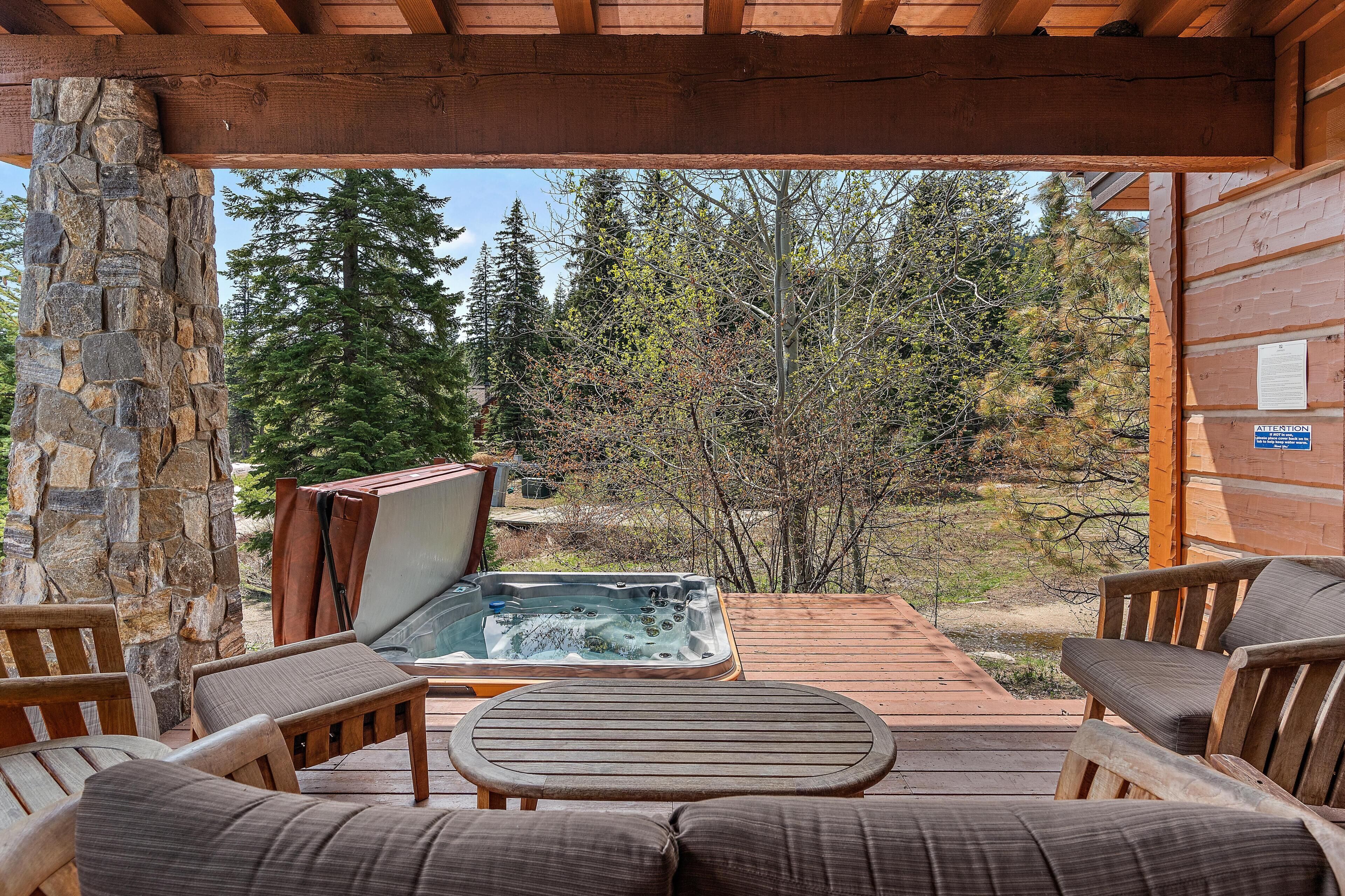 A wooden deck with a hot tub, stone wall, and wooden furniture.