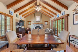 A spacious dining area with a wooden table and chairs, a fireplace, and large windows. - Wonderful Cottage |Ski In/Out | Private Hot Tub (Tamarack)