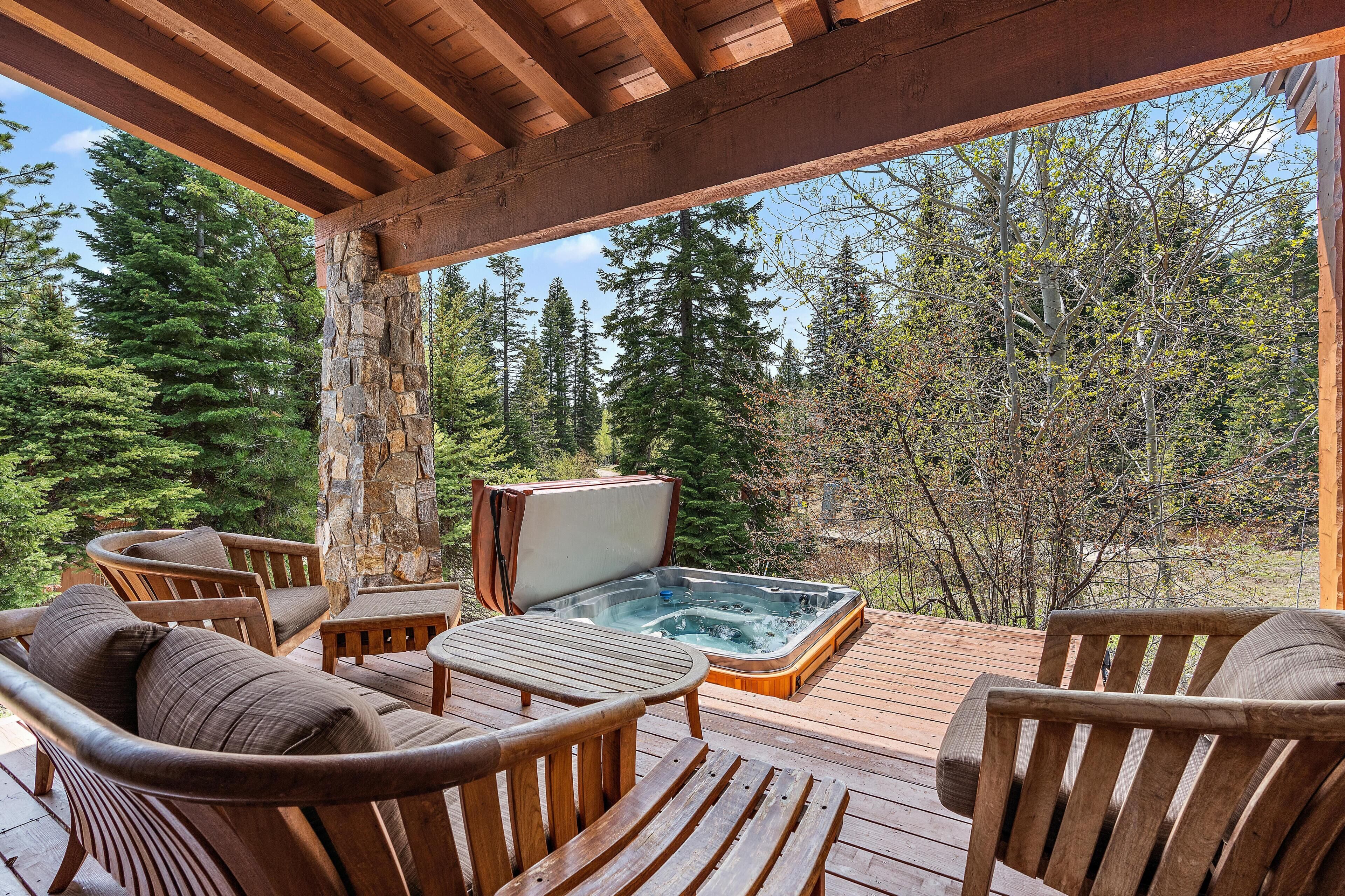 Una terraza de madera con un jacuzzi, mobiliario exterior y vista a un bosque.
