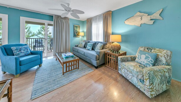 Un salon avec un canapé bleu, un fauteuil bleu et un fauteuil à motifs. On y trouve une table basse, une lampe et un décor mural représentant des poissons.