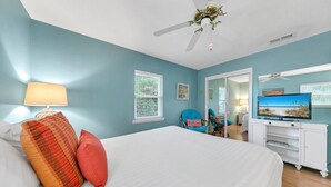 Une chambre à coucher avec un lit, une télévision, un ventilateur de plafond et une fenêtre avec des stores.