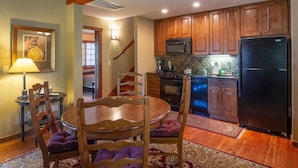 Una cocina con armarios de madera, un refrigerador negro, un microondas y una estufa. Hay una mesa de comedor con sillas y una lámpara.
