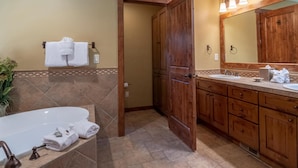 Un baño con bañera, dos lavamanos, armarios de madera y un espejo grande.