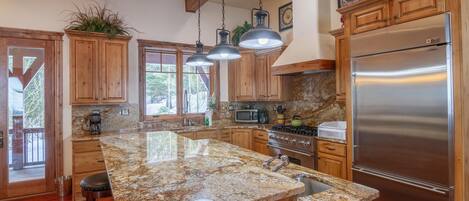 Cocina con gabinetes de madera, encimeras de granito, electrodomésticos de acero inoxidable y lámparas colgantes.