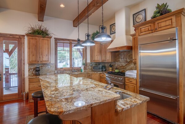 A kitchen with wooden cabinets, granite countertops, stainless steel appliances, and hanging pendant lights.