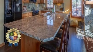 A spacious kitchen with wooden cabinets, a granite countertop, and a large island with bar stools. - Beautiful Townhome|Private Hot Tub, Wood Fireplace (Tamarack)