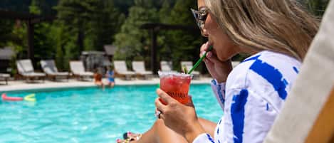 Una persona descansando junto a una piscina, con sillones de descanso y sombrillas al fondo.