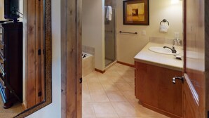 A bathroom with a wooden vanity, a glass shower enclosure, a painting on the wall, and a television in the corner. - Beautiful Townhome|Private Hot Tub, Wood Fireplace (Tamarack)