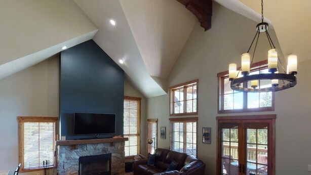 A spacious living room with a stone fireplace, a large TV mounted on the wall, and a chandelier. - Beautiful Townhome|Private Hot Tub, Wood Fireplace (Tamarack)