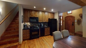 Une cuisine avec des meubles de rangement en bois, un four à micro-ondes, une cuisinière et un réfrigérateur. On y trouve une table à manger avec des chaises, ainsi qu’un escalier menant à une autre pièce.