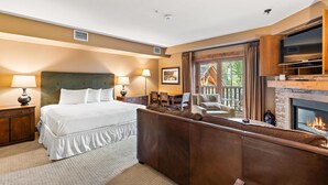 A hotel room with a large bed, a fireplace, a TV, and a view of the outdoors. - Unique King Studio  with Jet Tub (Tamarack)
