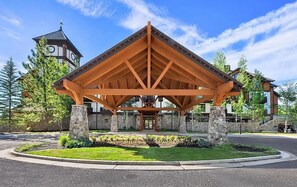 A wooden pavilion with a stone base, surrounded by a landscaped area with trees and a building with a clock tower in the background. - Unique King Studio  with Jet Tub (Tamarack)