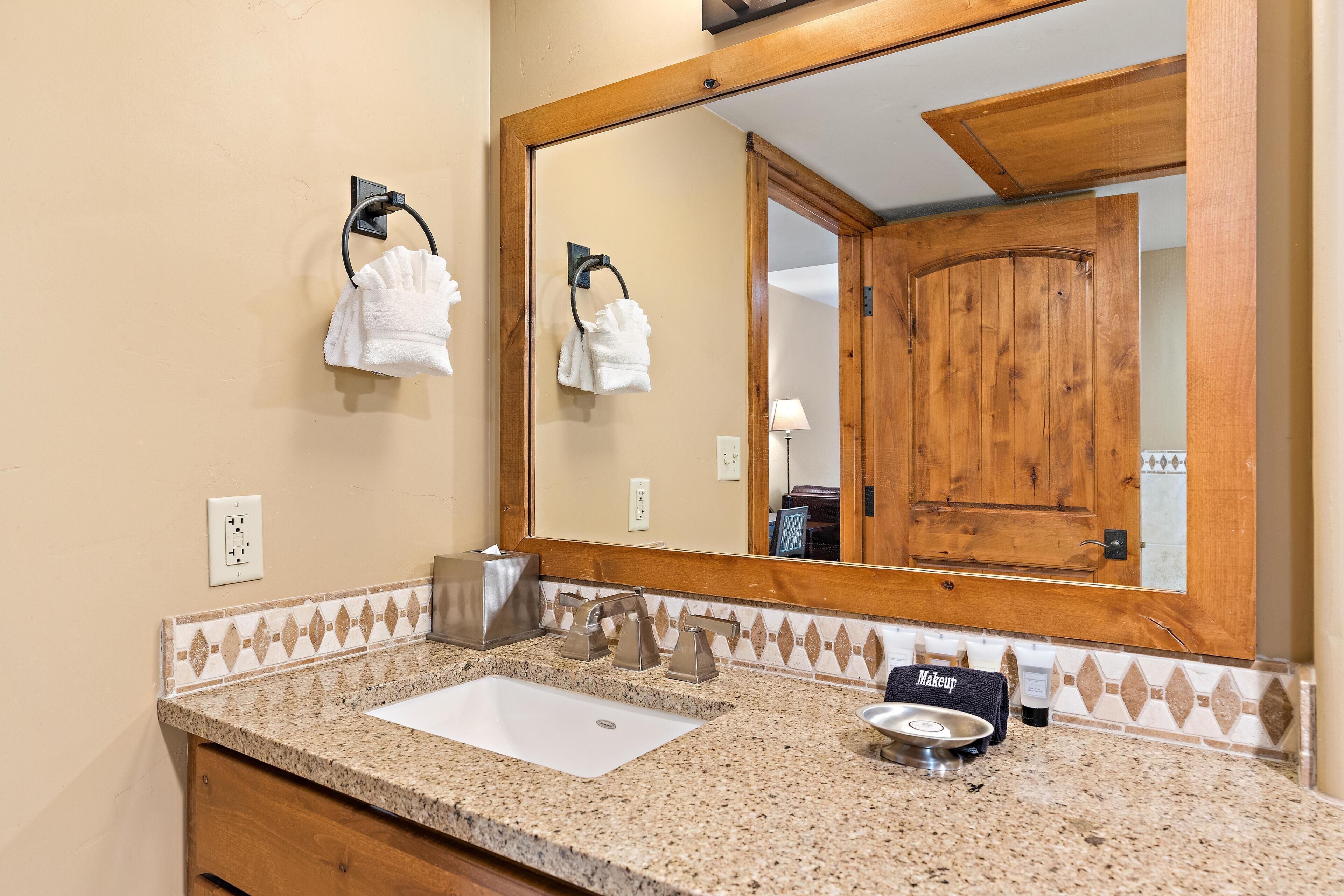 Baño con lavamanos, toallero, espejo y puerta de madera.