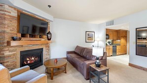 A living room with a fireplace, a sofa, a coffee table, and a TV mounted on a brick wall. - Mountainside Studio with Fireplace and Jet Tub (Tamarack)
