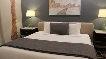 A hotel room with a bed, two bedside tables, lamps, a painting on the wall, and a brick wall feature.