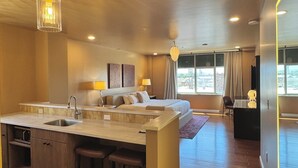 A modern hotel room with a kitchen area, a large bed, and a desk.