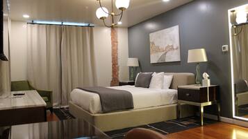 A hotel room with a bed, bedside tables, a desk, a chair, a mirror, and a chandelier.