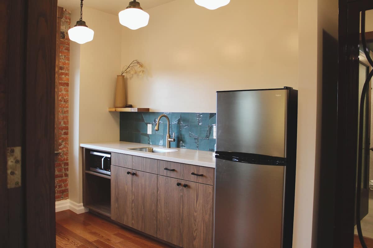A modern kitchen with wooden cabinets, a stainless steel refrigerator, a built-in oven, and a tiled backsplash.