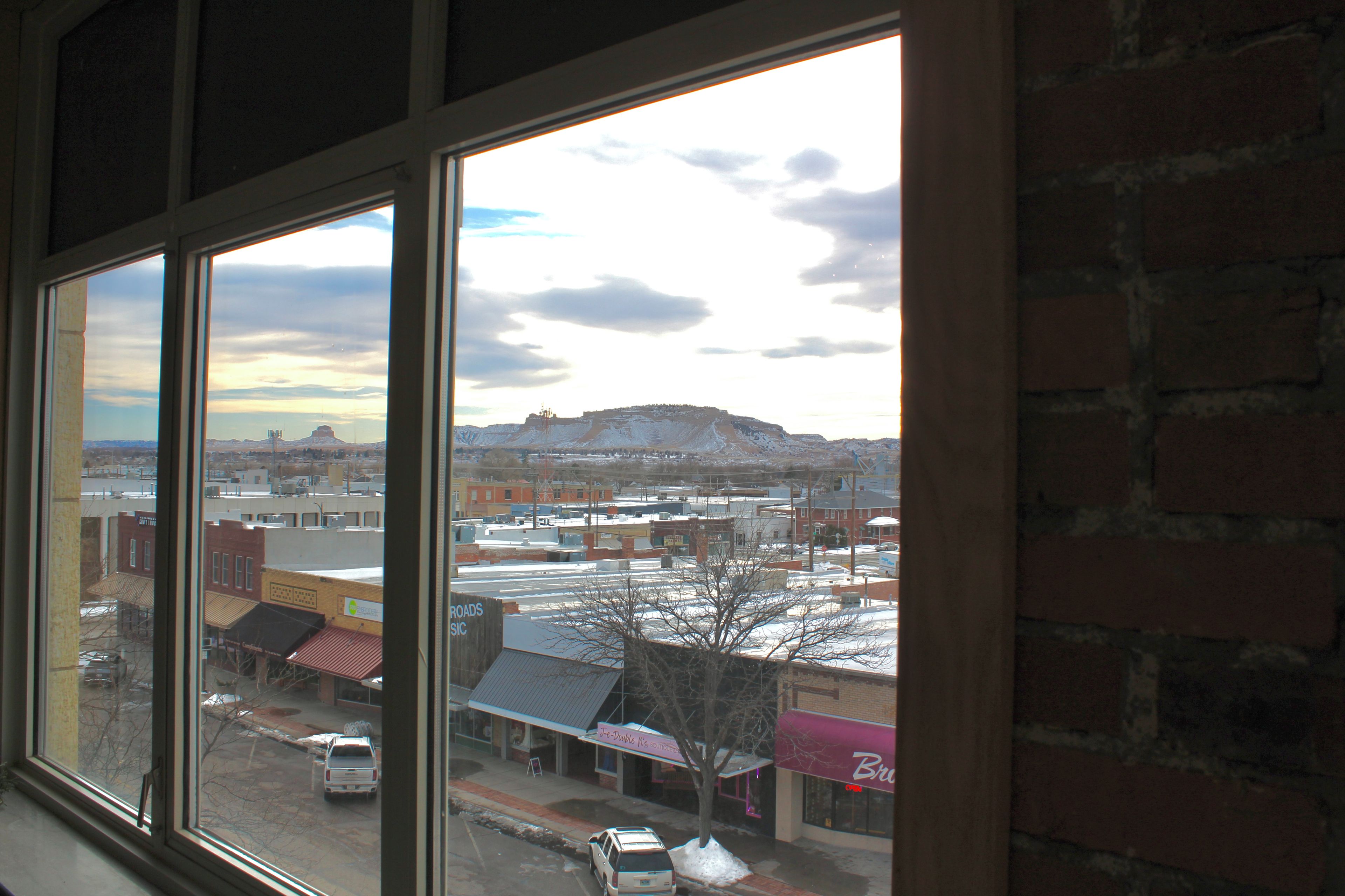 A view through a window of a street with buildings, a tree, and a distant hill.