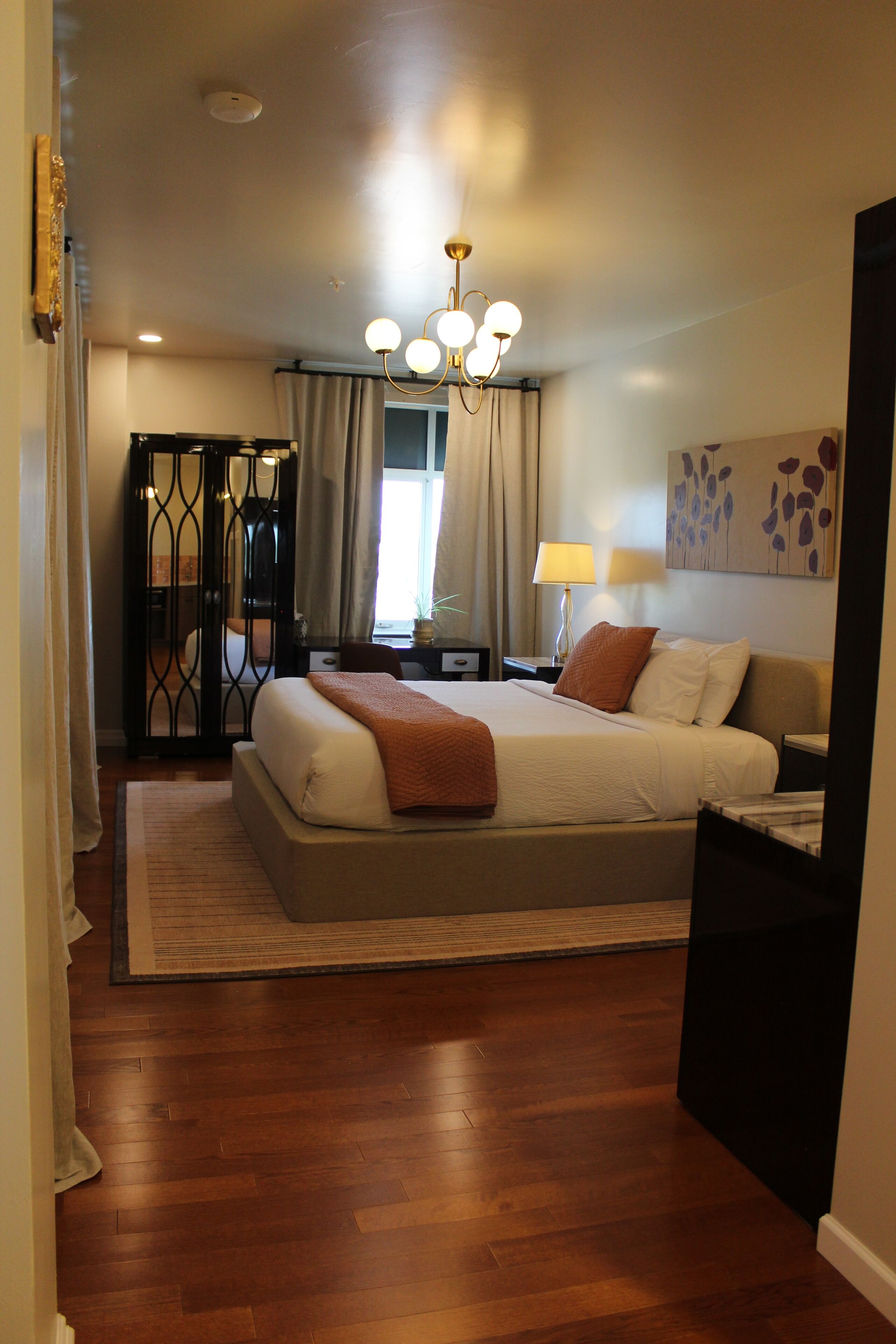 A bedroom with a large bed, a nightstand, a lamp, a painting, and a wardrobe.