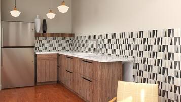 A modern kitchen with wooden cabinets, a stainless steel refrigerator, and a patterned backsplash. There are three pendant lights hanging above the counter.