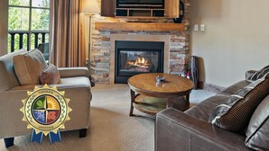 Una sala de estar con chimenea de piedra, un televisor de pantalla plana montado sobre ella, un sofá, una mesa de centro y vistas al exterior a través de una ventana.