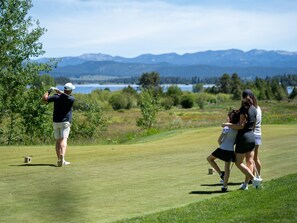 Un campo de golf con un jugador a punto de golpear una bola, un cadí y una mujer caminando a su lado.