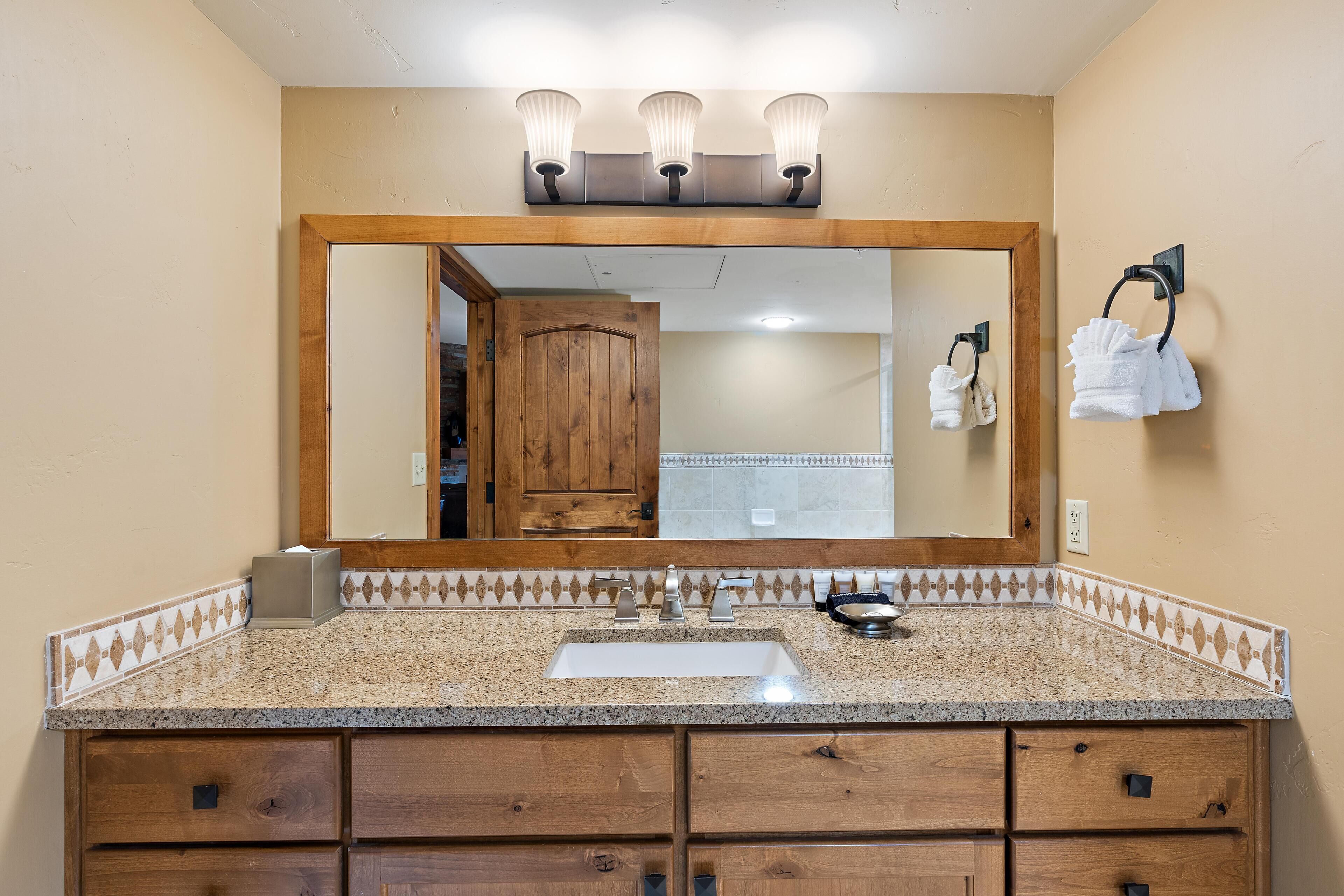 Baño con tocador de madera, lavamanos y espejo con tres luces.