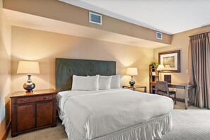 Une chambre d’hôtel avec un grand lit, deux tables de chevet avec des lampes, un bureau avec une chaise et un tableau au mur.