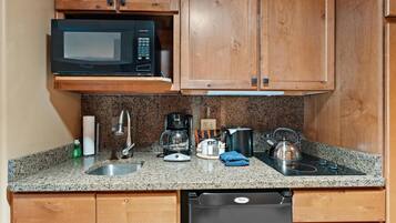 A kitchen with wooden cabinets, a microwave, a coffee maker, a kettle, and a dishwasher.