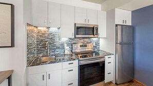 Una cocina moderna con armarios blancos, un refrigerador de acero inoxidable, un microondas integrado y un salpicadero de piedra.