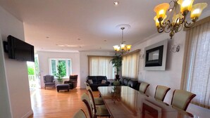 A spacious dining area with a long table and chairs, a chandelier, and a television mounted on the wall. - Comfortable stay in a large home on the shores of Lake Erie (Dunnville)