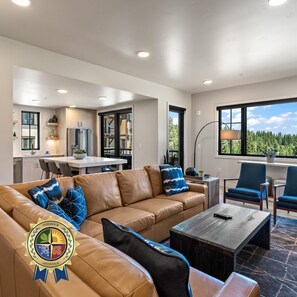 A modern living room with a leather sofa, a coffee table, and a view of a kitchen and dining area.