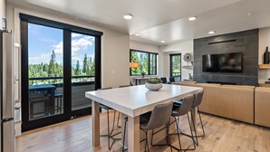 Una cucina moderna con un'isola grande, una TV a schermo piatto e una porta scorrevole in vetro che dà su un balcone con vista sugli alberi.