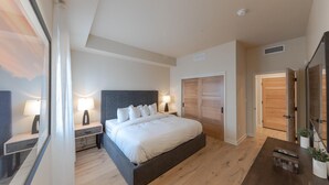 A modern bedroom with a large bed, bedside tables, a wardrobe, and a desk with plants.
