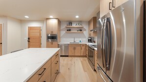 A modern kitchen with a large island, stainless steel appliances, wooden cabinets, and a white countertop.