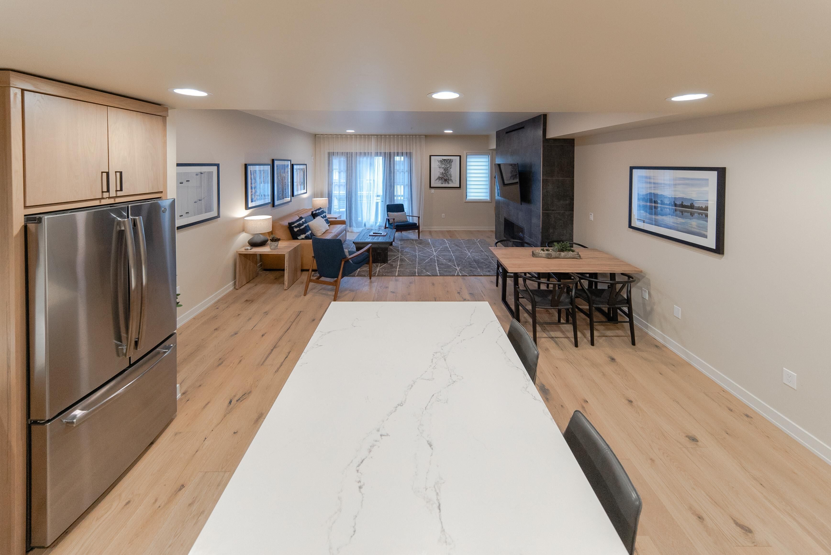 A modern kitchen with a large island, wooden cabinets, and a stainless steel refrigerator.